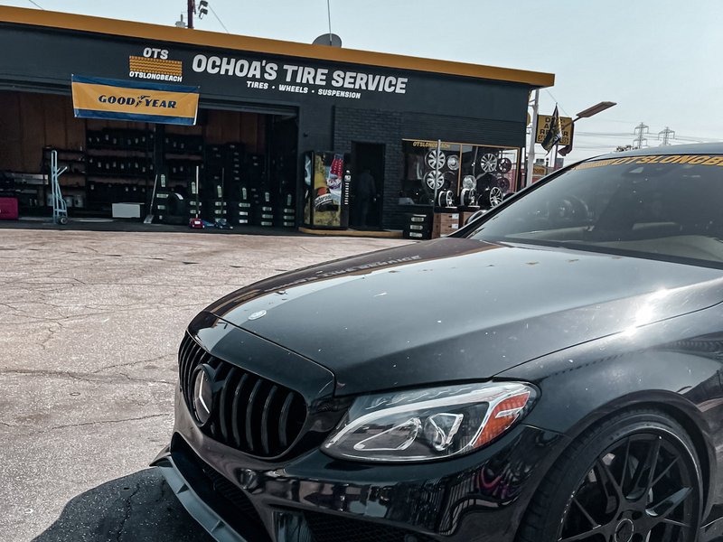 Ochoa's Tire Service Paramount location — yellow OTS signage, checkered pennant flags, open service bay with wheels and tires visible inside